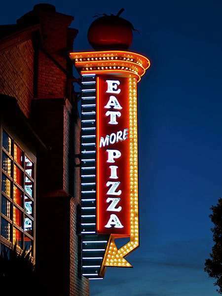 A close up shot of the Toppers "Eat More Pizza" neon sign with casino lighting.